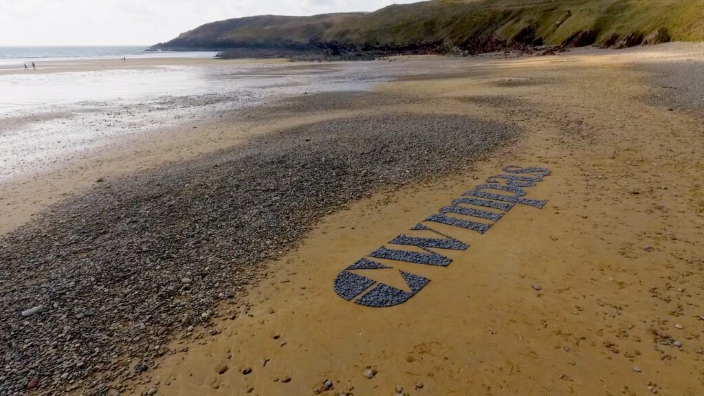 The Cwmpas logo reading Cwmpas made in stones on a beach.